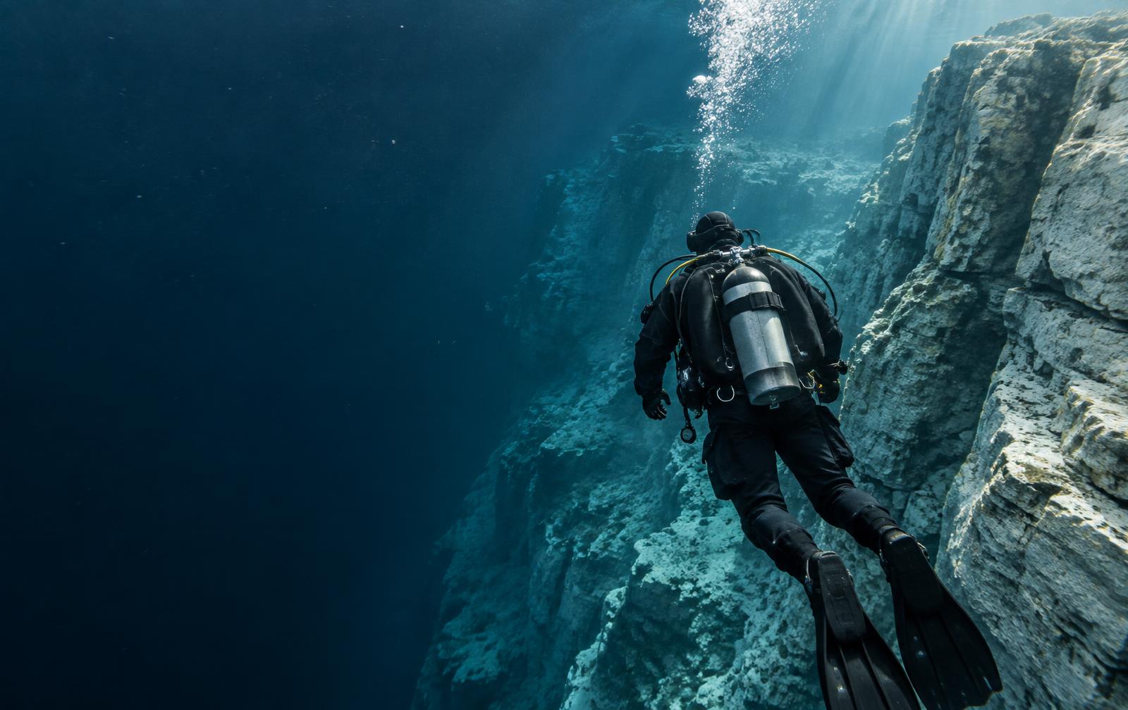 Recreational diver descending beside an underwater limestone wall